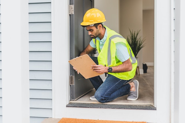 contractor%20in%20a%20yellow%20hard%20hat%20and%20vest%20inspecting%20a%20homes%20exterior